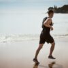 man wearing black tank top and running on seashore