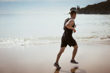 man wearing black tank top and running on seashore