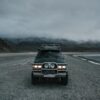 car parked on seashore near mountains in foggy weather