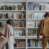 woman in brown coat standing in front of books