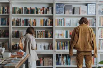 woman in brown coat standing in front of books