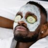 a man relaxing with a cream on his face and sliced cucumber on his eyes