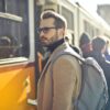 man in brown coat and gray backpack posing for a photo